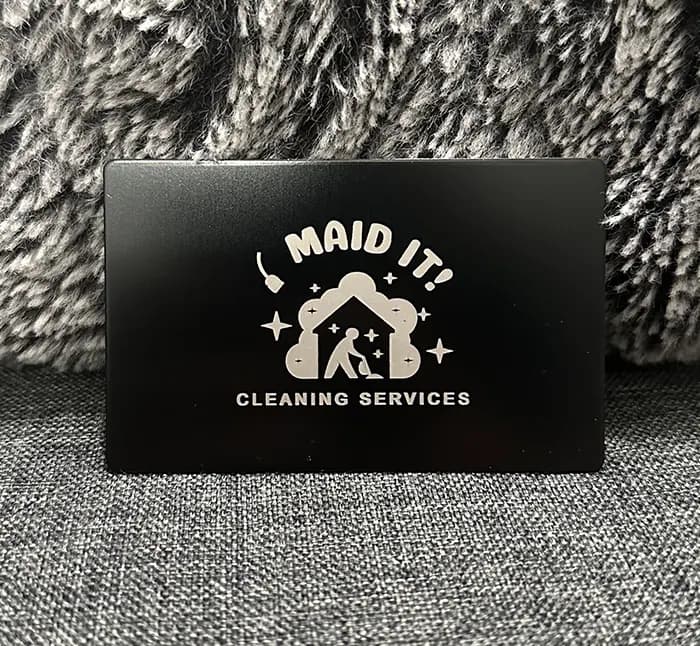 A finished I Maid It Cleaning Services metal card photographed on textured fabric